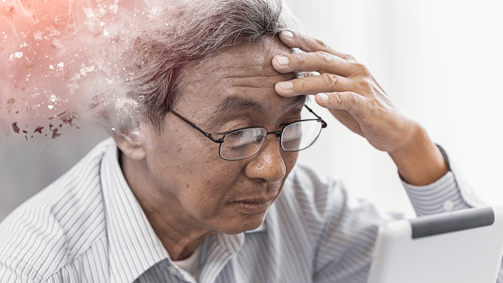 An older man of Asian descent grasps his head with his hand, representing aphasia resulting from Alzheimer's disease.