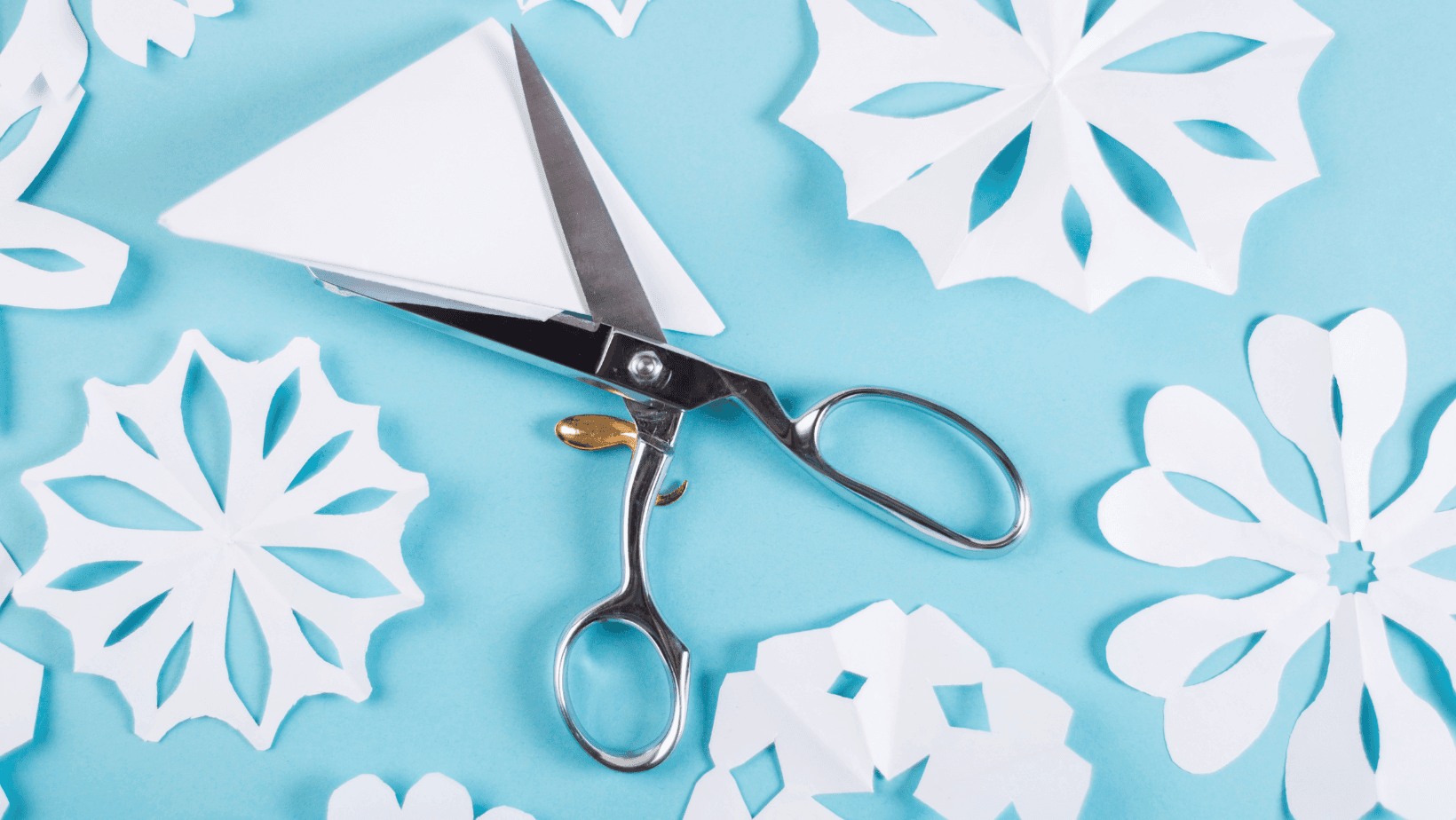 scissors resting on a blue table with coffee filter snowflakes
