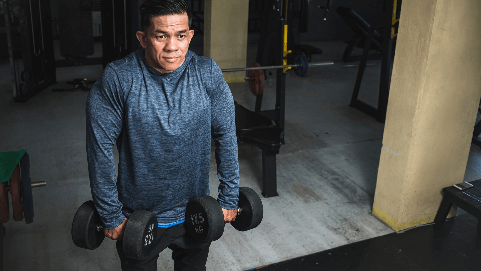 A man in the gym lifting two weights performing the exercise shoulder shrugs