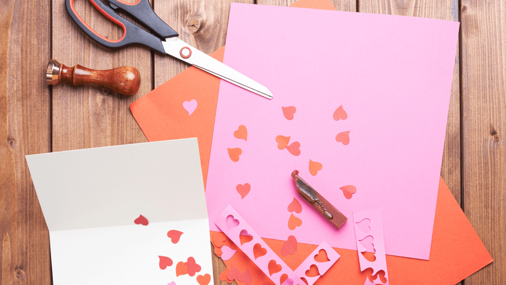 valentines day cards being made, pink and red papers resting on a table with a pair of scissors