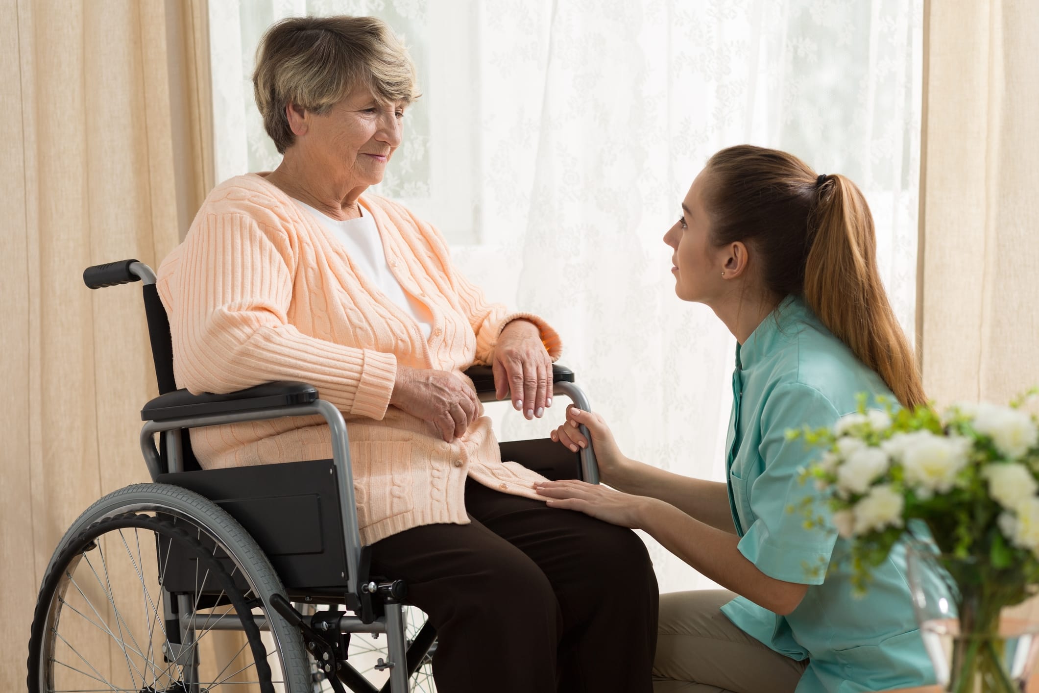 Woman Caregiver helps elderly woman in wheel chair